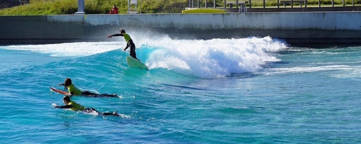 Drei Surfer*innen surfen auf einer künstlichen Welle in einem Surfpark